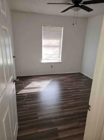 an empty room with wooden floor fan and windows