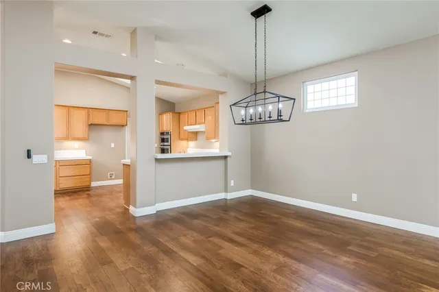 a view of an empty room with window wooden floor and a kitchen view