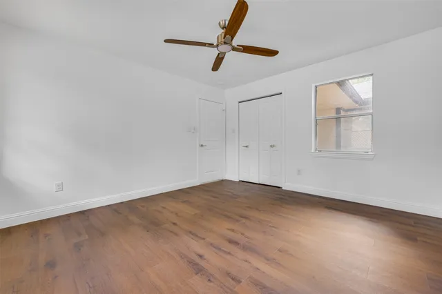 an empty room with wooden floor ceiling fan and windows
