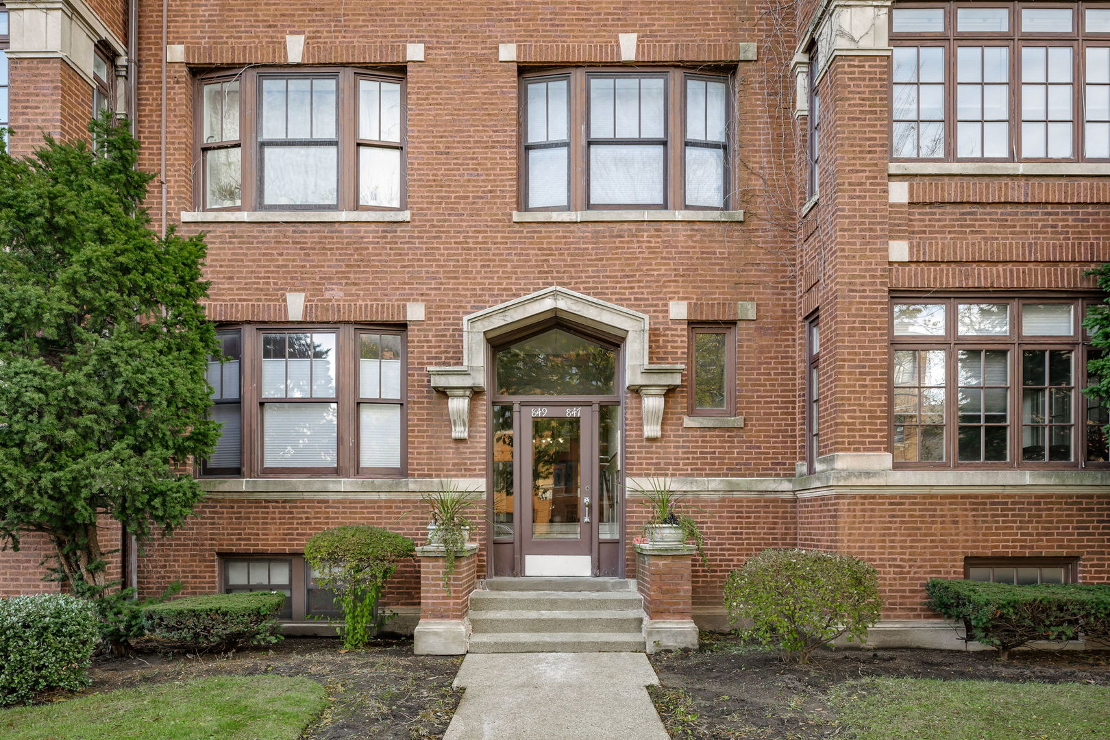 a front view of a brick building plants and large trees
