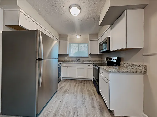 a kitchen with stainless steel appliances granite countertop a refrigerator a stove a sink and white cabinets with wooden floor