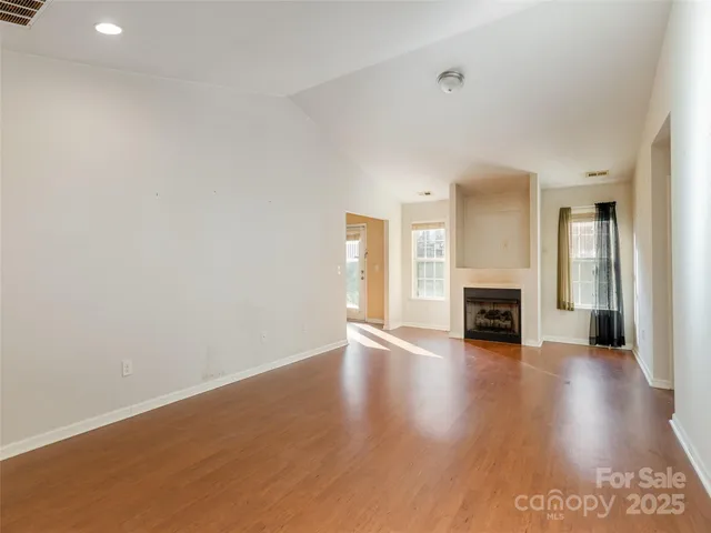 a view of an empty room with wooden floor fireplace and a window