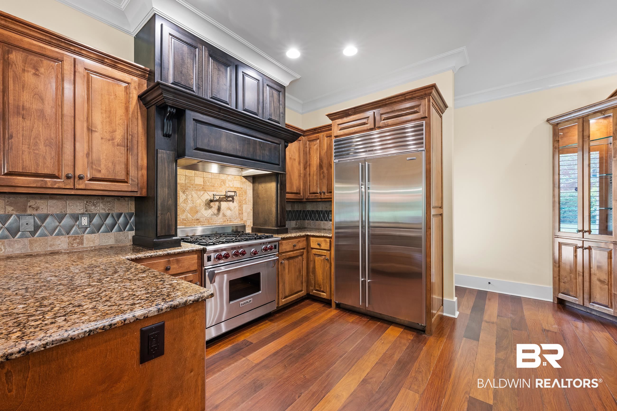 30463 Dolive Ridge Daphne, AL 36527 - Photo 37 of 58 Gourmet kitchen featuring a stainless steel range and refrigerator, rich wood cabinetry, granite countertops, and hardwood flooring