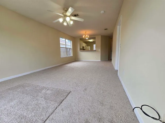 an empty room with chandelier fan and windows