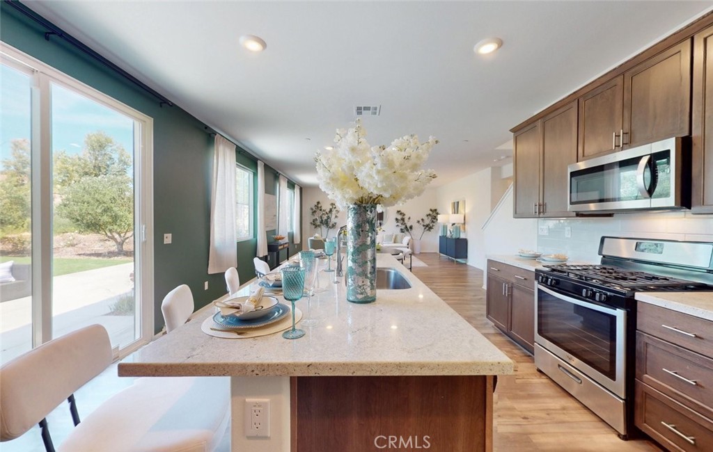 24320 Insignia Drive Menifee, CA 92584 - Photo 22 of 65 a kitchen with stainless steel appliances granite countertop a stove a refrigerator a sink dishwasher a dining table and chairs with wooden floor