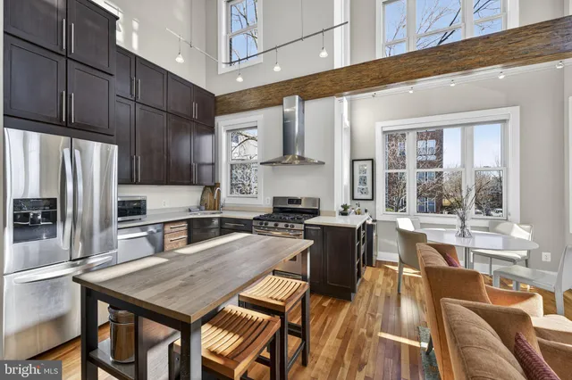 a kitchen with stainless steel appliances granite countertop a stove a refrigerator a sink a dining table and chairs with wooden floor