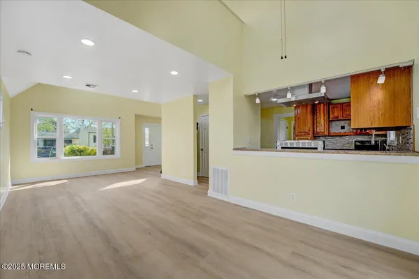 an empty room with kitchen view and wooden floor
