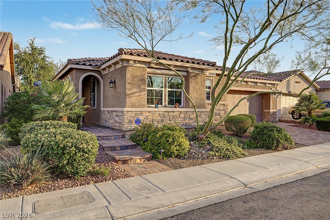 7415 Campbell Ranch Avenue Las Vegas, NV 89179 - Photo 10 of 52 A terracotta tile roof crowns this home with a stone and stucco facade, complemented by a paver walkway and lush landscaping.