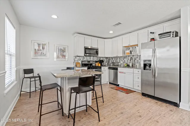 a kitchen with stainless steel appliances kitchen island granite countertop a refrigerator a stove a sink a dining table and chairs with wooden floor