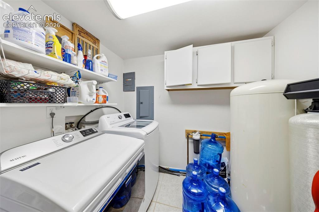 13075 Blaney Road South Peyton, CO 80831 - Photo 26 of 40 Dedicated laundry area featuring a washing machine and dryer, white wall-mounted storage cabinets, open shelving, and a water softener/whole house filter.