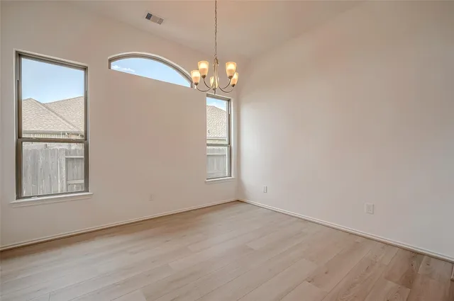an empty room with wooden floor chandelier and windows