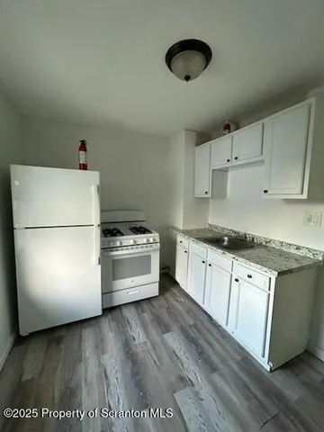 a kitchen with granite countertop a refrigerator a stove a sink and white countertops with wooden floor