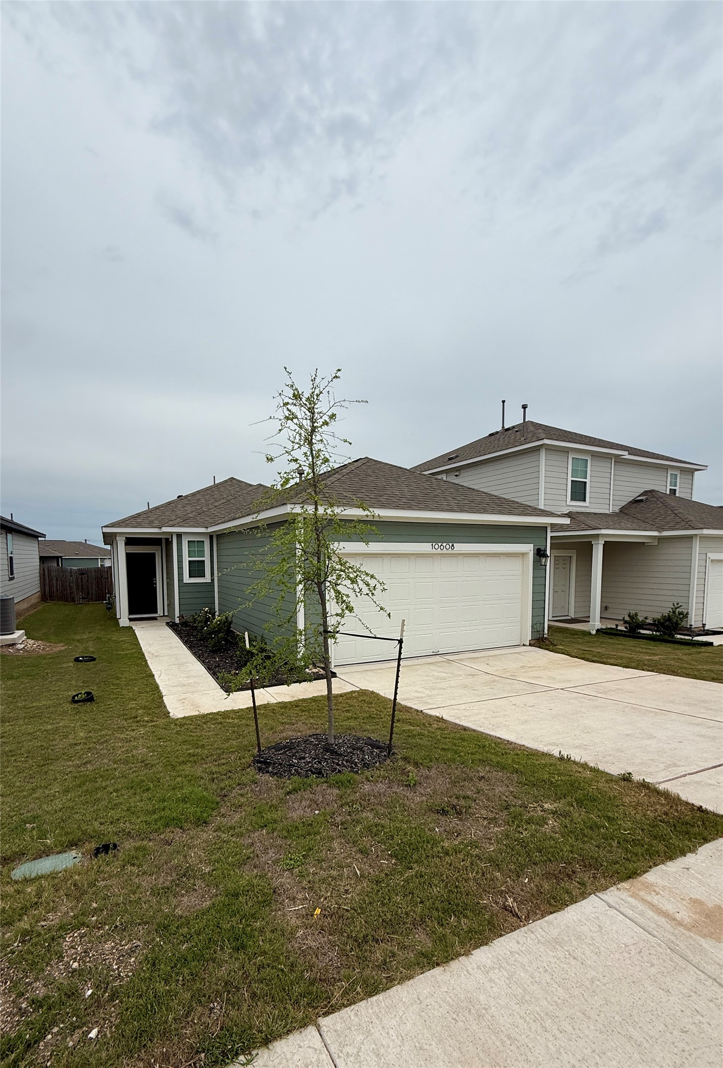 10608 Ridan Way Buda, TX 78610 - Photo 1 of 1 Single-story residence featuring a two-car garage, light green siding, and a dark brown shingle roof