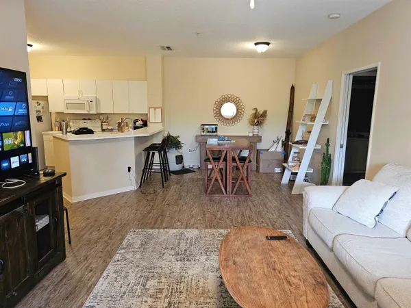 a living room with couches a coffee table and kitchen view with wooden floor