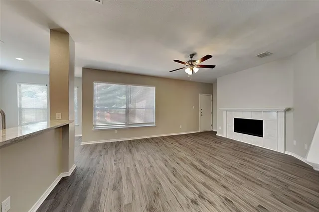 an empty room with wooden floor chandelier fan and windows