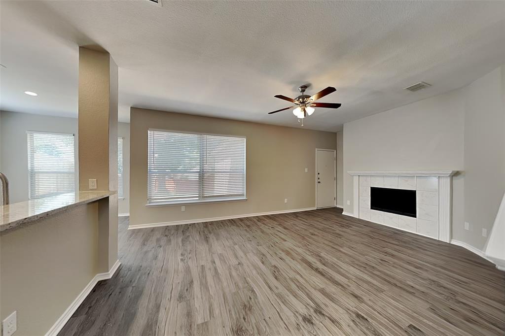 1202 Dove Brook Drive Allen, TX 75002 - Photo 3 of 23 Unfurnished living room with a tiled fireplace, wood finished floors, healthy amount of natural light, and a ceiling fan