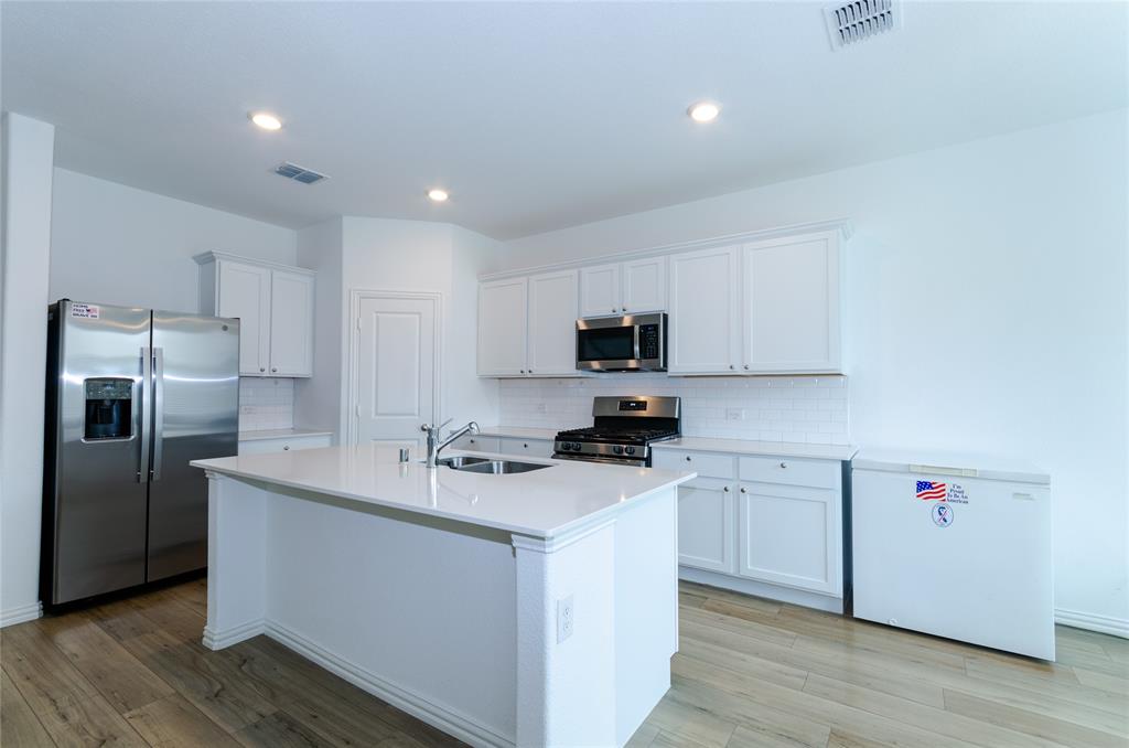 1222 Sequoia Lane Princeton, TX 75407 - Photo 3 of 29 Kitchen featuring stainless steel appliances, a sink, light wood finished floors, backsplash, and white cabinets