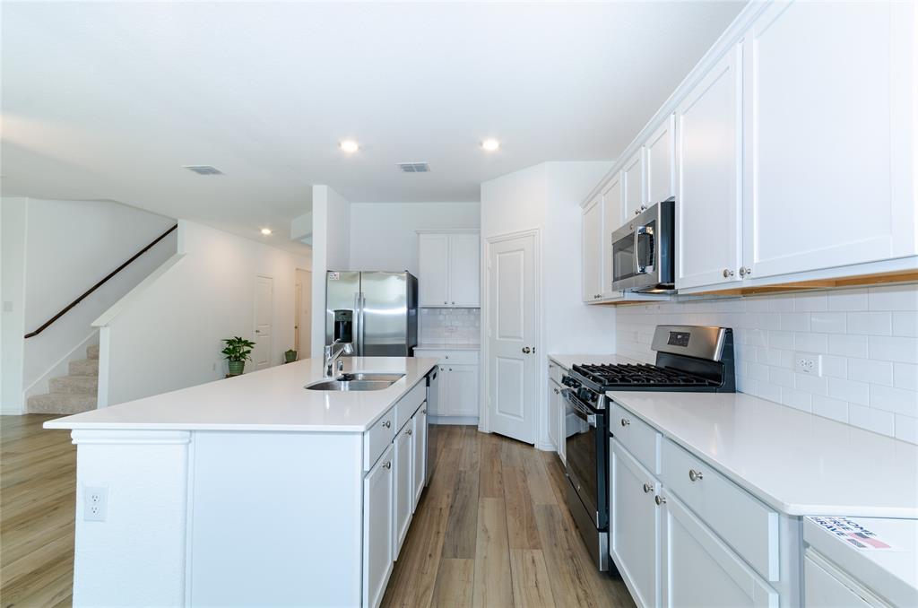 1222 Sequoia Lane Princeton, TX 75407 - Photo 4 of 29 Kitchen featuring appliances with stainless steel finishes, a sink, light wood-style floors, a center island with sink, and decorative backsplash