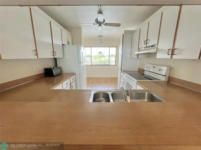 a kitchen with stainless steel appliances a stove a sink a refrigerator white cabinets and couches
