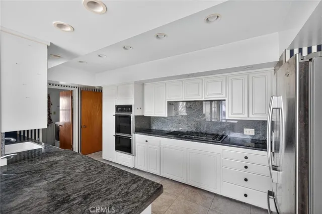 a kitchen with granite countertop a refrigerator and white cabinets