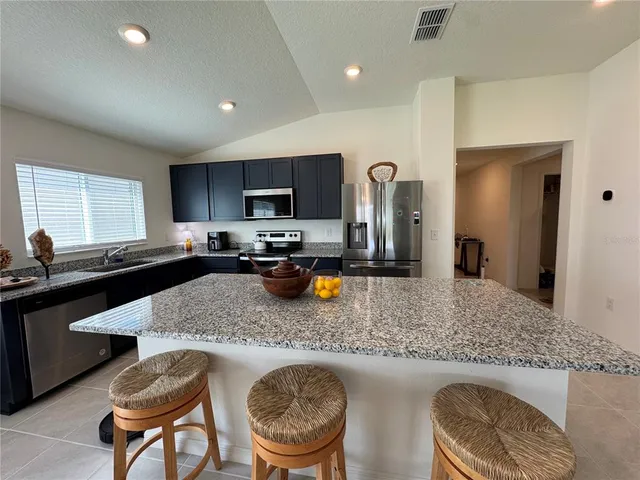 a kitchen with stainless steel appliances granite countertop a sink a stove a refrigerator a dining table and chairs