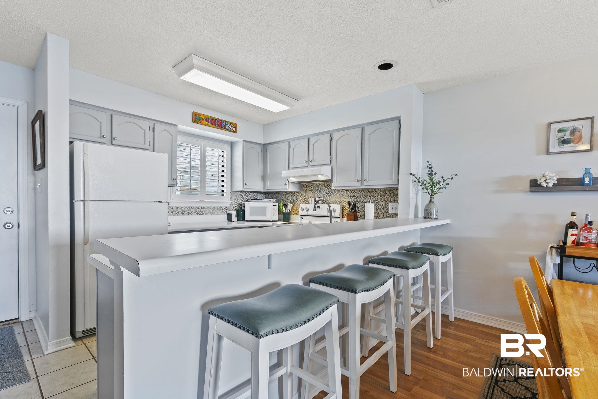 25861 Canal Road, Unit 78 Orange Beach, AL 36561 - Photo 11 of 45 Kitchen featuring white appliances, a peninsula, gray cabinetry, under cabinet range hood, and backsplash