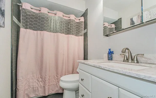 a bathroom with a granite countertop sink vanity mirror and toilet