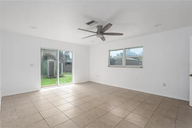 a view of an empty room with window and chandelier fan