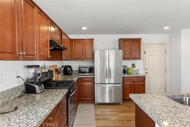 a kitchen with stainless steel appliances kitchen island granite countertop wooden floor cabinets dining table and chairs