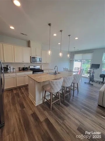 a open kitchen with stainless steel appliances granite countertop a stove a refrigerator a kitchen island a dining table and chairs with wooden floor
