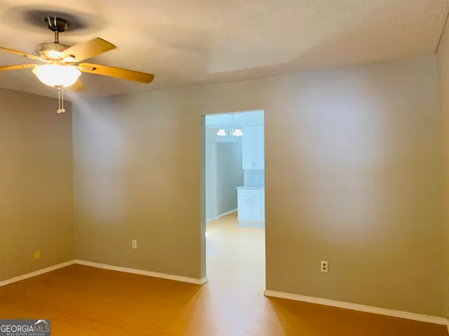 an empty room with a chandelier fan and wooden floor