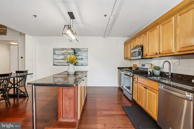 a kitchen with stainless steel appliances a stove a sink dishwasher a refrigerator white cabinets and wooden floor