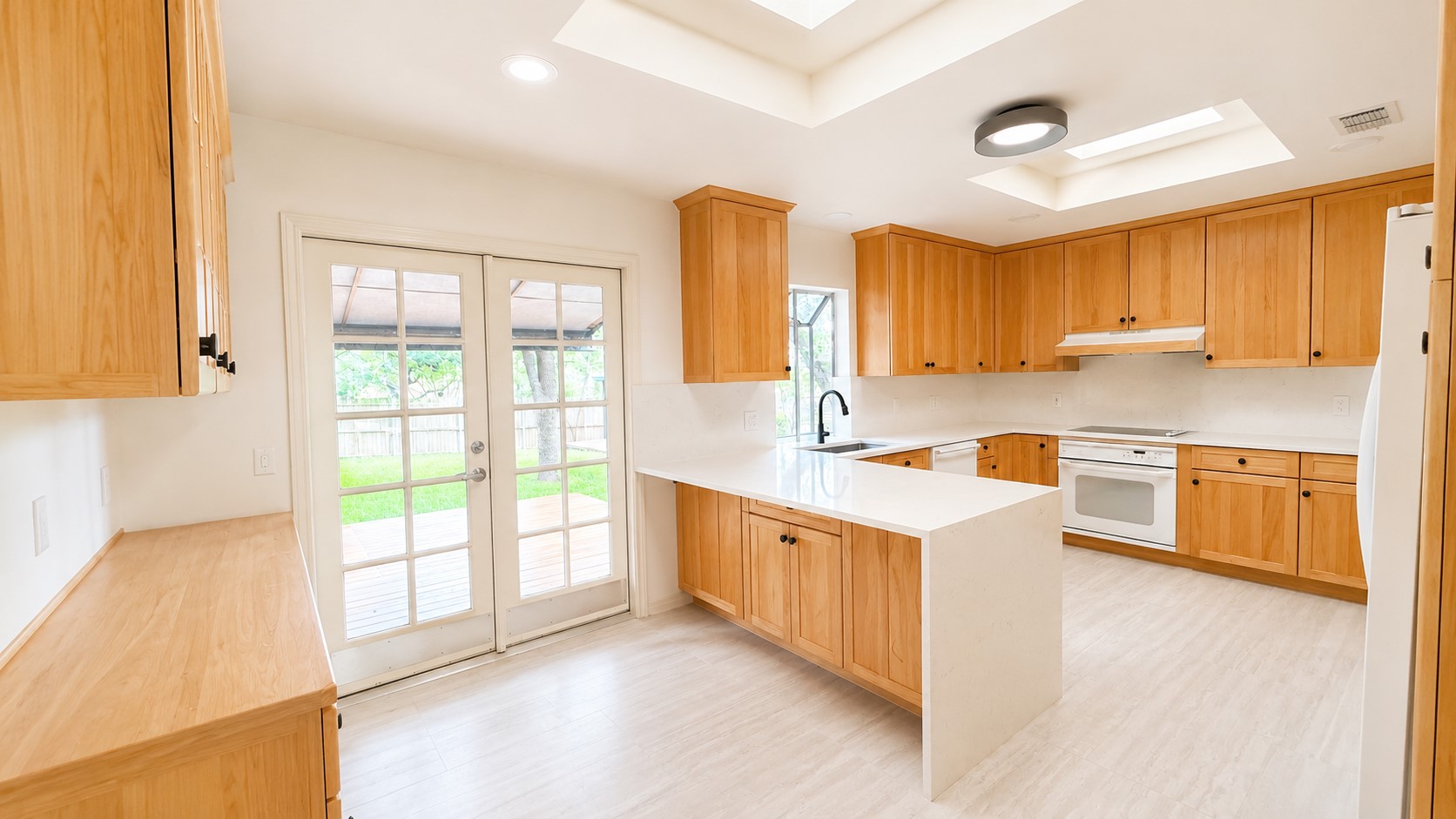 405 Ridgewood Road Austin, TX 78746 - Photo 7 of 22 Kitchen featuring light wood cabinetry, white countertops, built-in appliances, a central island, and dual skylights