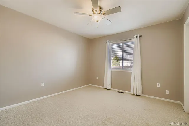 an empty room with chandelier fan and windows
