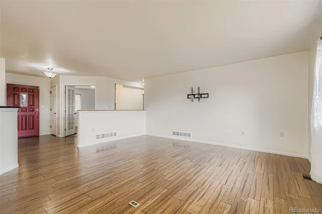 an empty room with wooden floor and a kitchen view