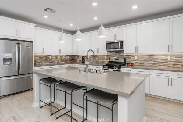 a kitchen with stainless steel appliances a sink a stove a refrigerator cabinets and chairs
