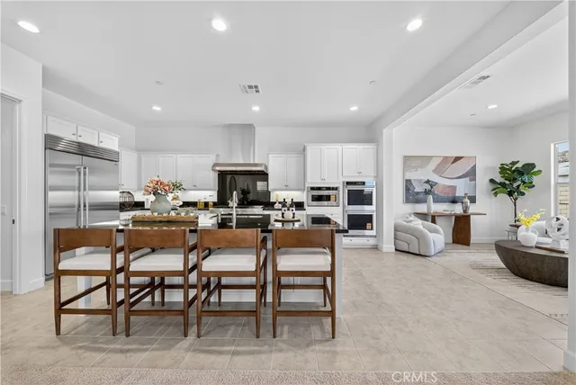 a kitchen with stainless steel appliances lots of white furniture a refrigerator a stove a sink a dining table and chairs