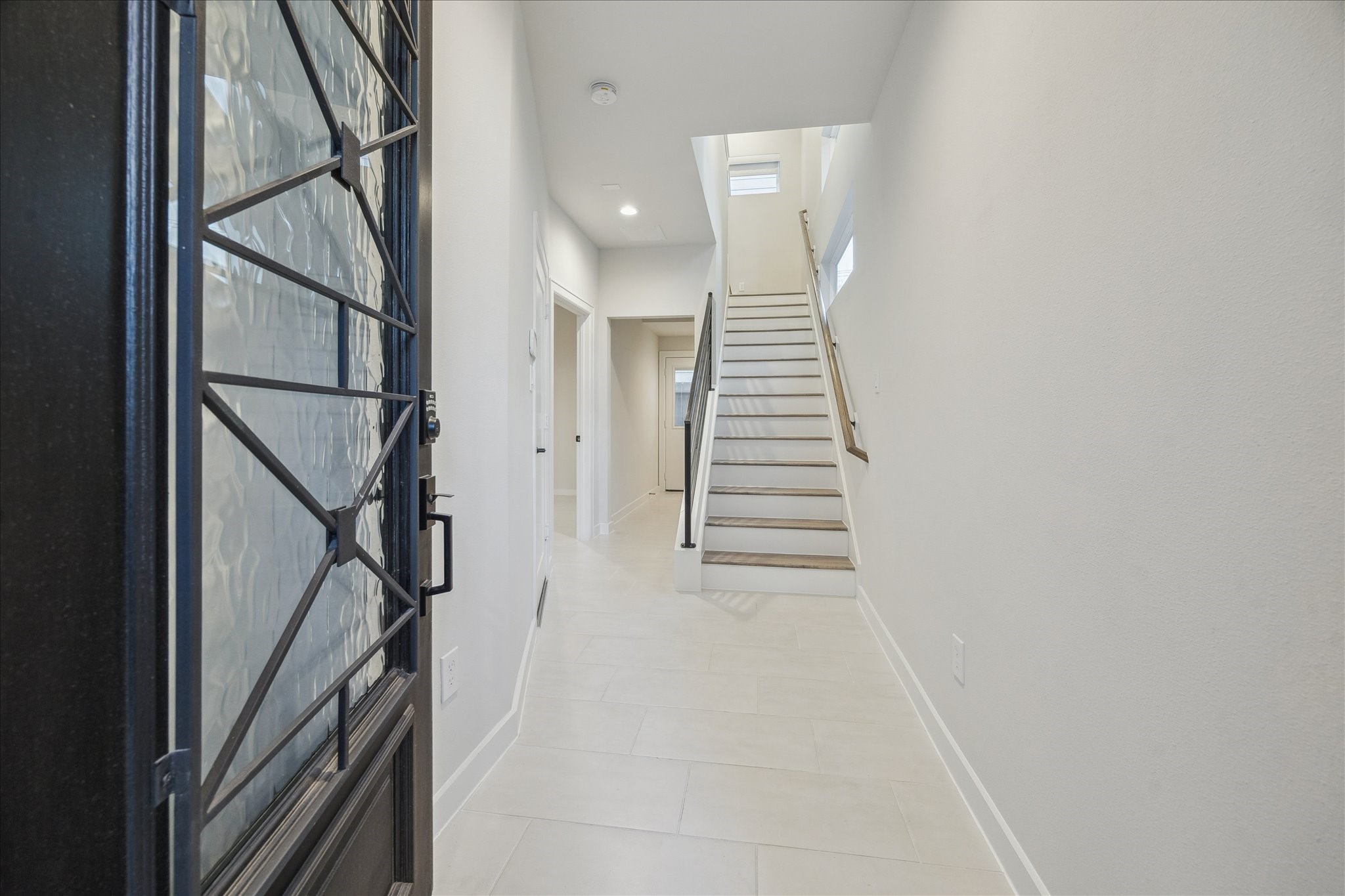 1603 Patterson Street, Unit E Houston, TX 77007 - Photo 5 of 32 Bright and inviting entryway with modern tile flooring, a stylish wrought iron front door, and a staircase leading upstairs. The hallway connects to various rooms, offering a spacious and welcoming first impression.