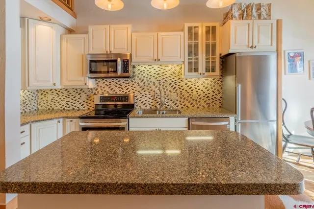 a kitchen with stainless steel appliances kitchen island granite countertop a refrigerator stove and white cabinets