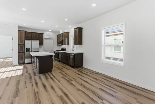 a kitchen with stainless steel appliances kitchen island granite countertop a sink dishwasher a stove and a refrigerator with wooden floor