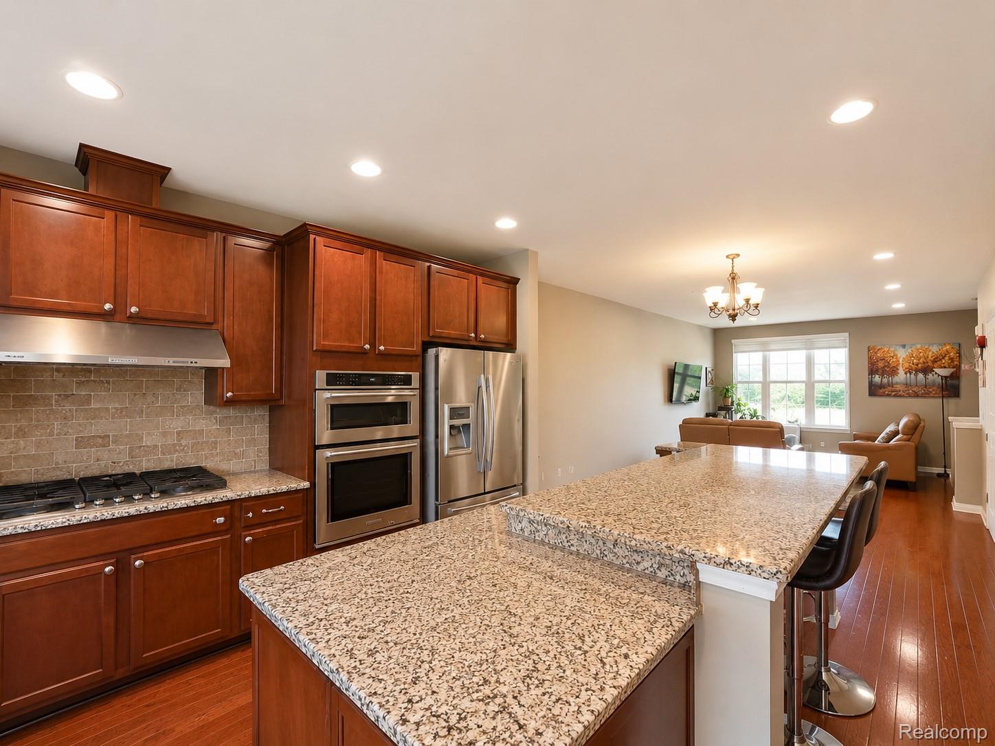 915 Barclay Circle Rochester, MI 48307 - Photo 6 of 14 Kitchen featuring rich wood cabinetry, stainless steel appliances, speckled stone countertops, and a tiled backsplash