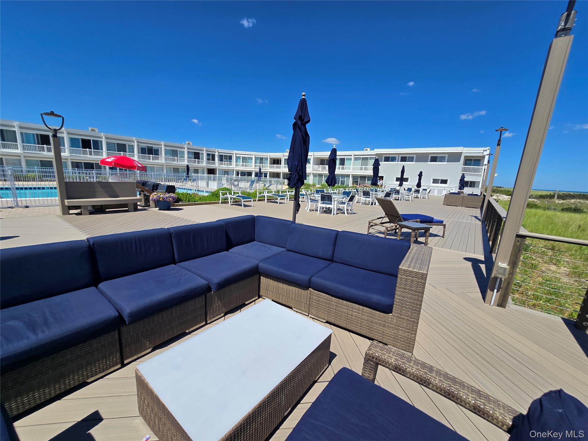 585 Dune Road, Unit L10 Westhampton, NY 11978 - Photo 9 of 25 Spacious outdoor deck area featuring a large sectional seating unit, a white rectangular coffee table, and a protective railing