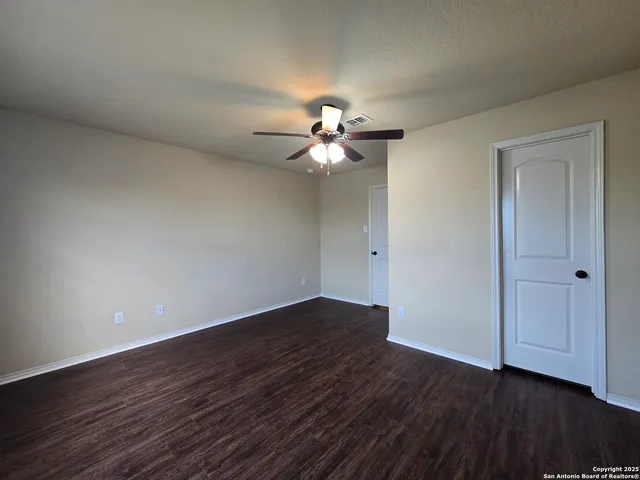a view of an empty room with wooden floor and a ceiling fan