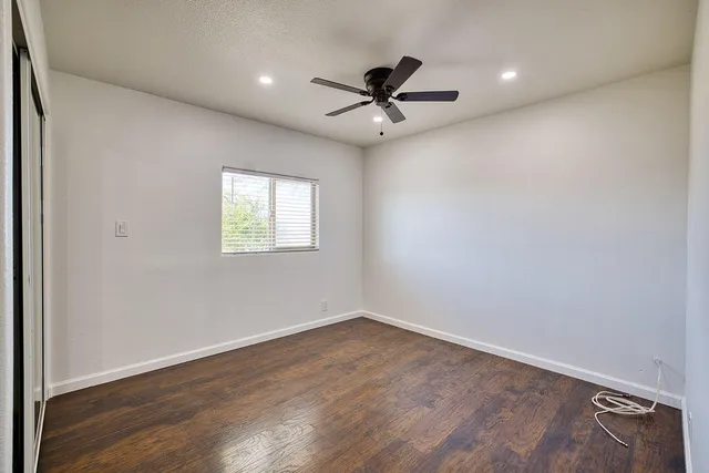 an empty room with wooden floor fan and windows