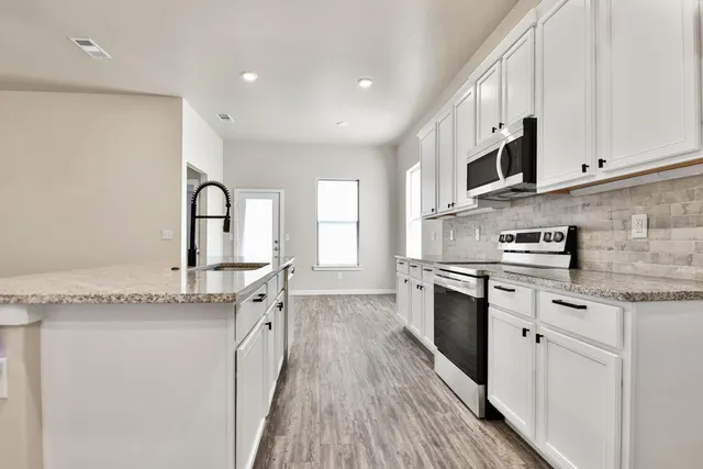 a kitchen with granite countertop a sink stainless steel appliances and white cabinets