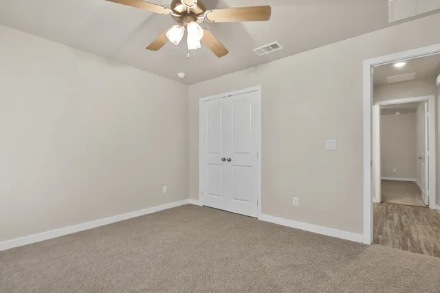 an empty room with a chandelier fan and closet area