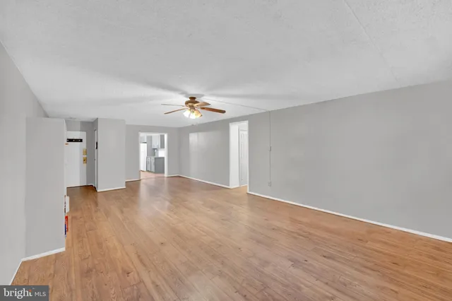 a view of an empty room with wooden floor and a ceiling fan