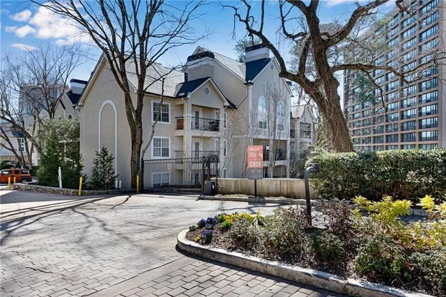 a view of a white house with a large tree and flower plants