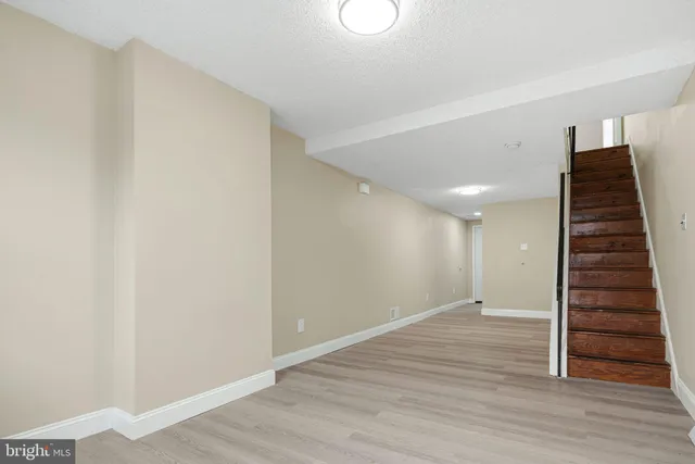 a view of an empty room with wooden floor stairs and a window
