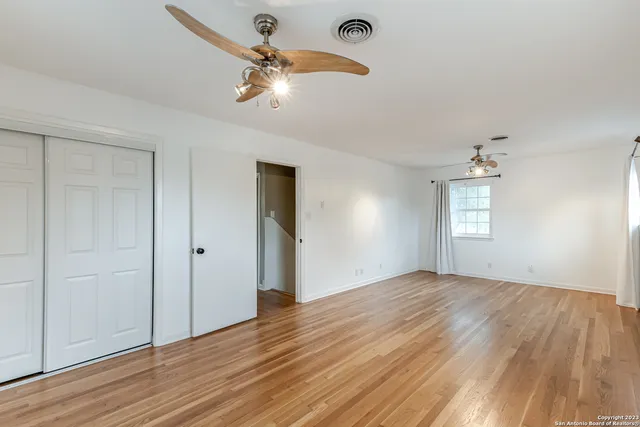 an empty room with wooden floor chandelier fan and windows
